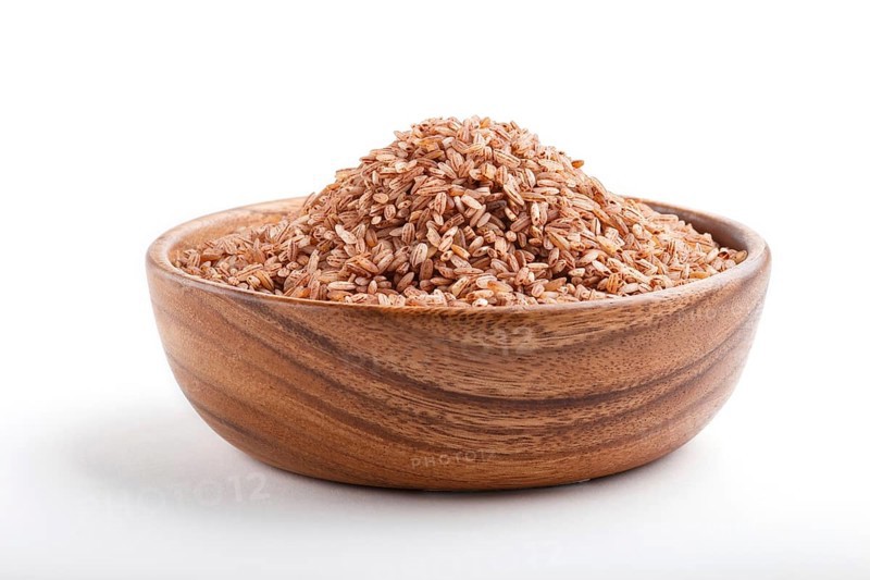 Wooden bowl with unpolished brown rice isolated on white background. Side view, close up