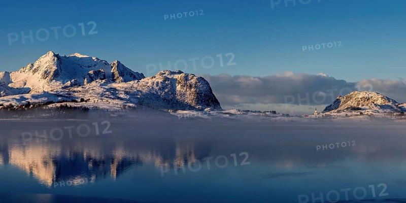 Leichter nebel in der verschneiten Berglandschaft auf den vesteralen mit schoener Spiegelung im Fjord