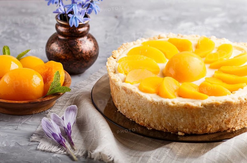 Round peach cheesecake and ceramic vase with blue flowers on a gray concrete background. side view, close up. linen napkin