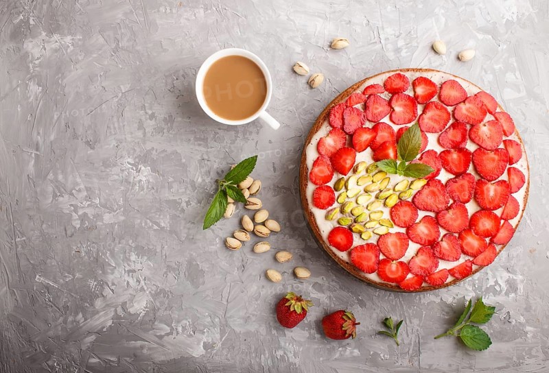 Homemade cake with yoghurt cream, strawberry, pistachio and a cup of coffee on a gray concrete background. top view. flat lay, copy space