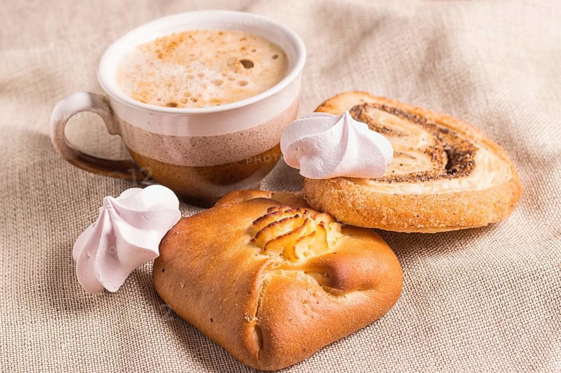 Sweet buns, meringues and coffee cup on a wooden board and linen tablecloth