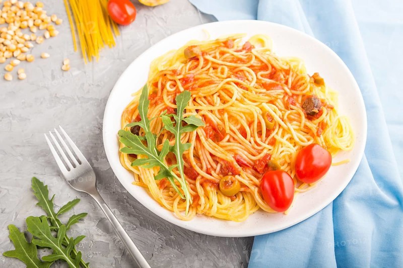 Corn noodles with tomato sauce and arugula on a gray concrete background and blue textile. Side view, close up, selective focus