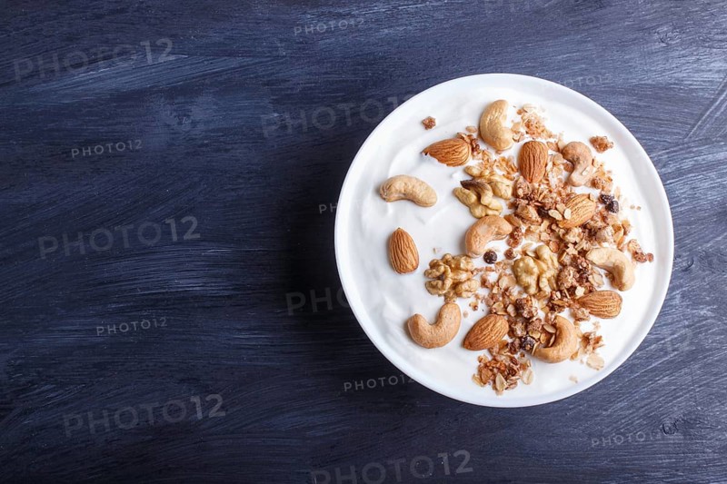 White plate with greek yogurt, granola, almond, cashew, walnuts on black wooden background. top view. copy space