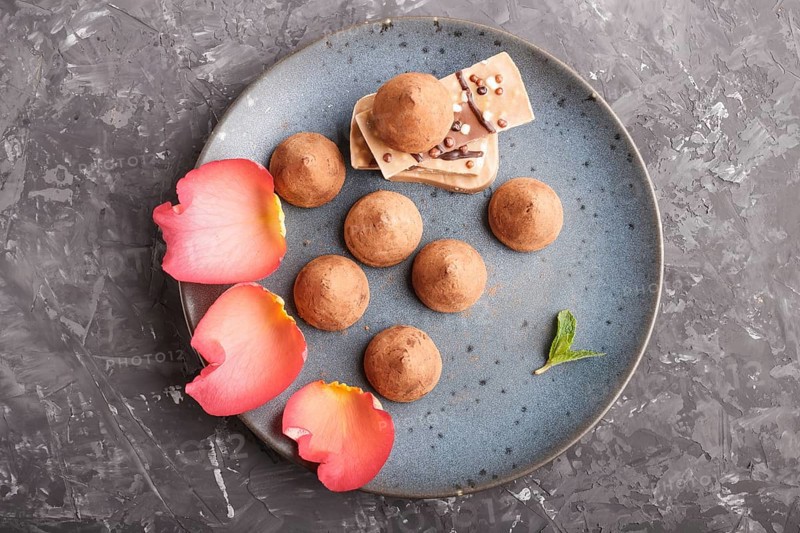 Chocolate truffle on blue ceramic plate decorated with rose petals on black concrete background. close up, top view