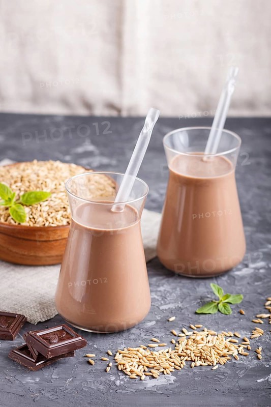 Organic non dairy oats chocolate milk in glass and wooden plate with oats seeds on a black concrete background. Vegan healthy food concept, close up, side view