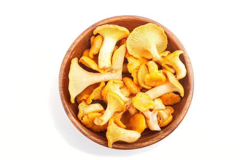 Bunch of chanterelle mushrooms in wooden bowl isolated on white background. top view, close up