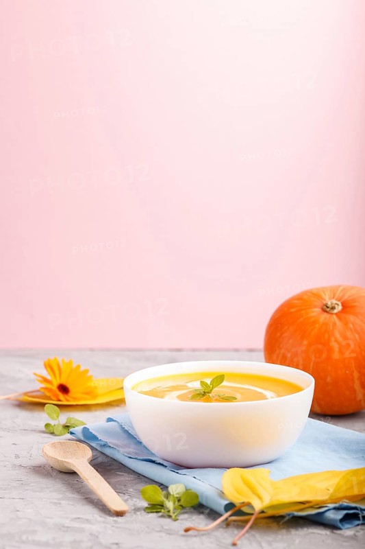 Traditional pumpkin cream soup with in white bowl on a gray and pink background with blue napkin. side view, close up, selective focus, copy space