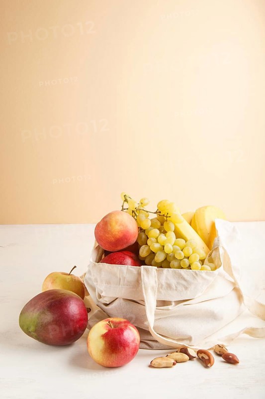 Fruits in reusable cotton textile white bag. Zero waste shopping, storage and recycling concept, eco friendly lifestyle. Side view, copy space. Peach, apple, mango, grape, banana