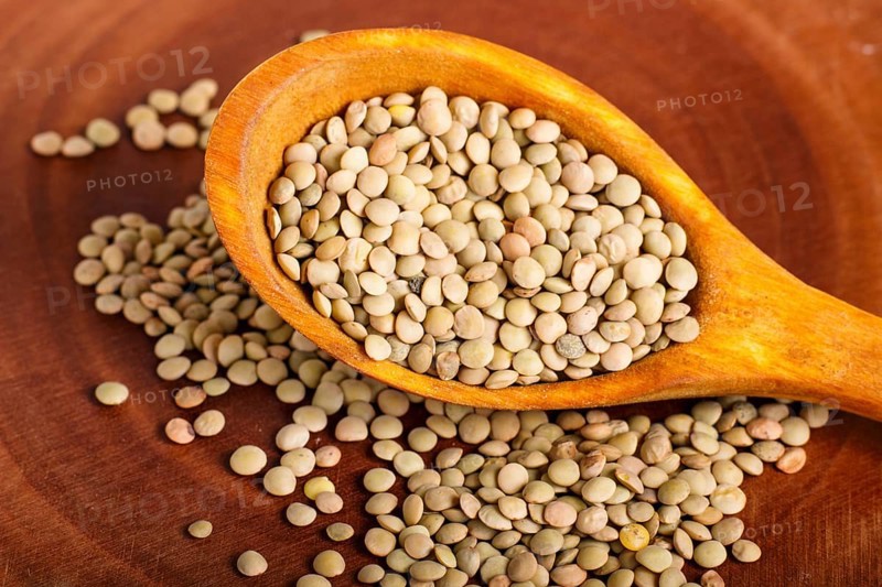 Pile of green lentils in a wooden spoon on brown background. Closeup