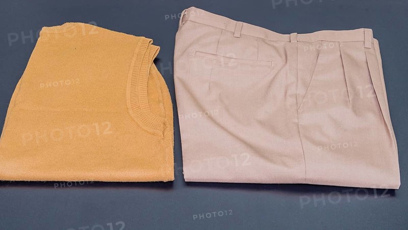 Brown sleeveless sweater next to pair of pleated beige pants on black background