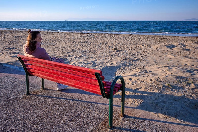 Young woman sitting on bench, bench, looking at the sea, coat, lonely, alone, beach, Peraia, also Perea, evening light, Thessaloniki, Macedonia, Greece, Europe