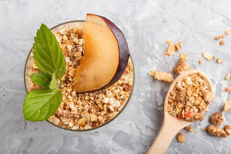 Yoghurt with plum, chia seeds and granola in a glass and wooden spoon on gray concrete background. top view, flat lay, close up
