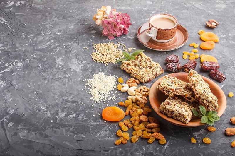 Homemade granola from oat flakes, dates, dried apricots, raisins, nuts with a cup of coffee on a black concrete background. Side view, copy space