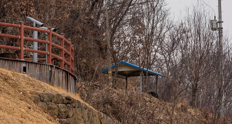 Wooden observation platform with two viewing binoculars behind red railing located in treed wilderness area in South Korea