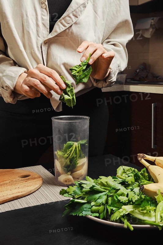 Hands of unrecognizable woman drop spinach into blender