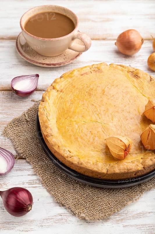 Autumn onion pie and cup of coffee on white wooden background and linen textile. Side view, close up