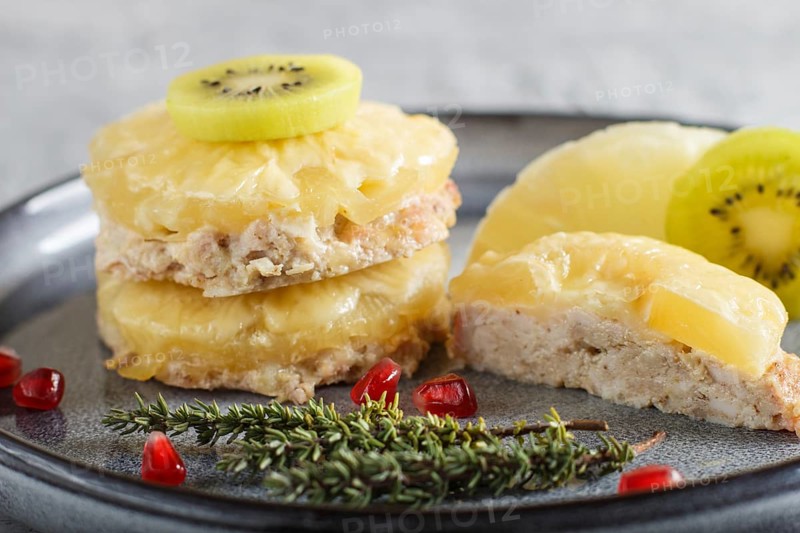 Pieces of baked pork with pineapple, cheese and kiwi on gray plate, side view, close up, selective focus