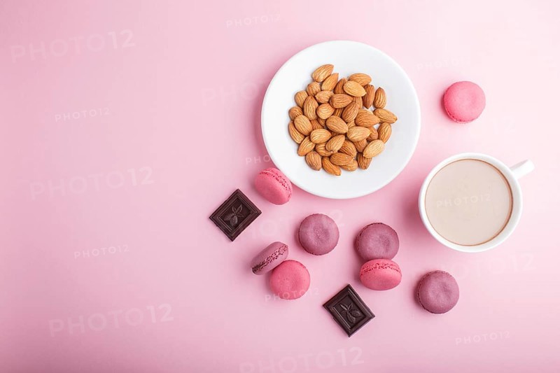 Purple and pink macaron or macaroon cakes with cup of coffee and almonds on pastel pink background. Morninig, spring, fashion composition. Flat lay, top view, copy space