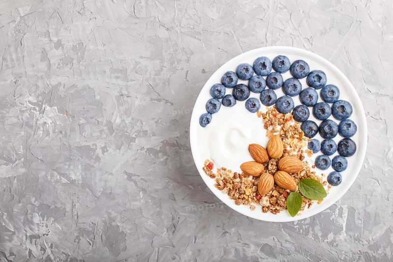 Yoghurt with blueberry, granola and almond in white plate on gray concrete background. top view, flat lay, copy space