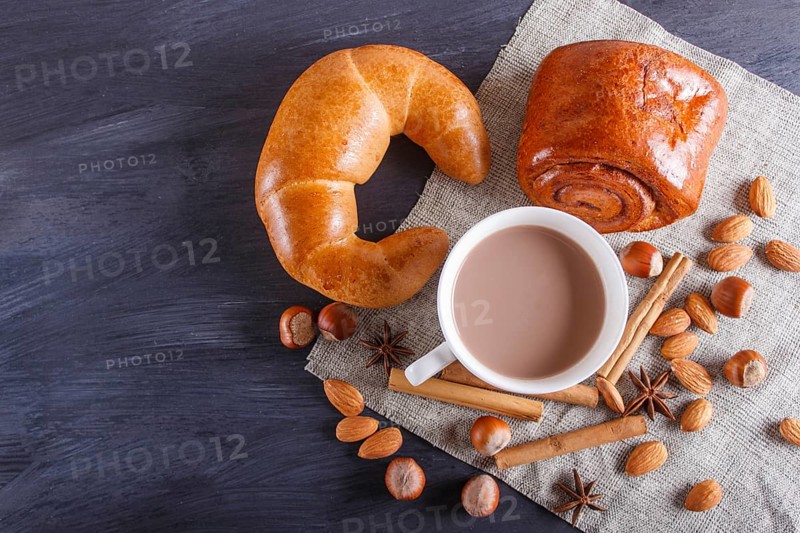 A cup of hot chocolate with nuts, buns and spices on linen napkin and black wooden background. copy space, top view