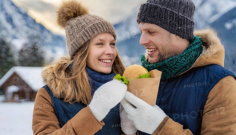 AI generated, human, humans, person, persons, man, woman, woman, 25, 30, years, two, outdoor, ice, snow, winter, seasons, eats, eat, drinks, drinking, cap, bobble hat, gloves, winter jacket, cold, cold, burger, hamburger, coffee to go, coffee, coffee mug