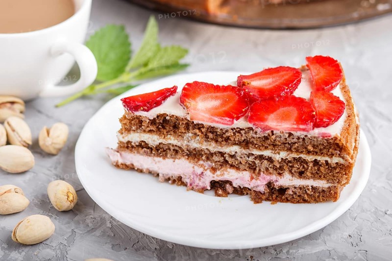 Homemade cake with yoghurt cream, strawberry, pistachio and a cup of coffee on a gray concrete background. side view, selective focus, close up