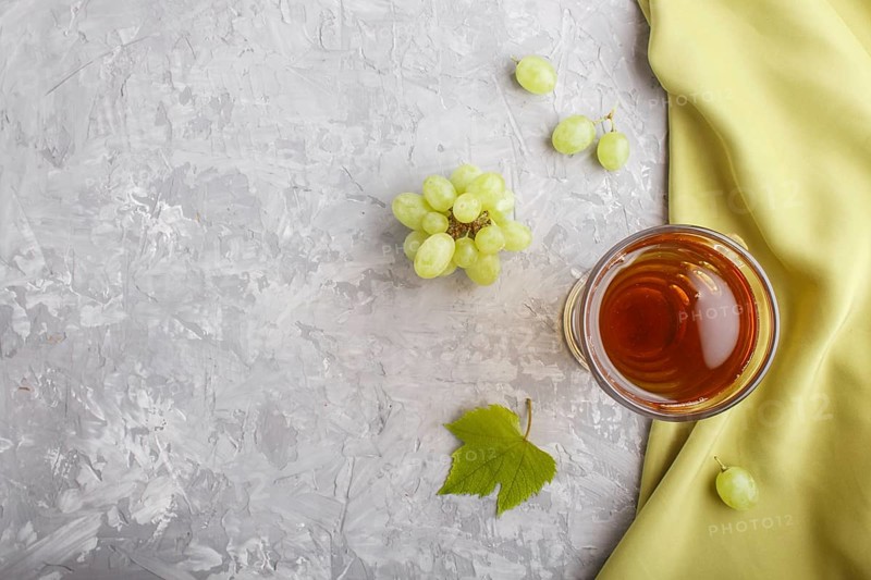 Glass of green grape juice with green textile on a gray concrete background. Morninig, spring, healthy drink concept. Top view, copy space, flat lay