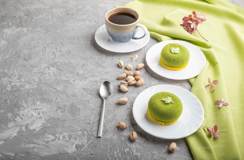 Green mousse cake with pistachio cream and a cup of coffee on a gray concrete background and green textile. side view, copy space