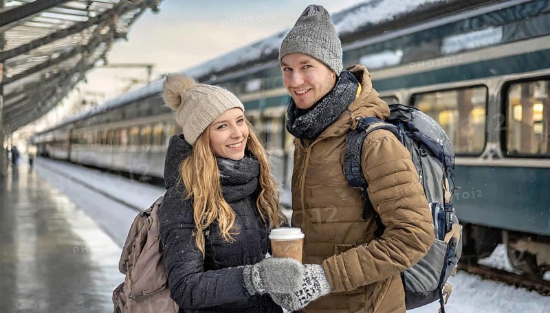 AI generated, woman, woman, man, men, A young couple wants to travel and is waiting for the train at the station, 25, 30, sneakers, shoes, sexy, attractive, attractive, long-haired, handbag, transport, traffic, backpack, bobble hat, coffee to go in hand, coffee, coffee cup, ice, winter, snow, two people sitting on the bench