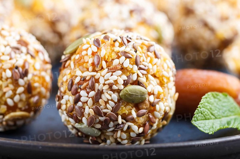 Energy ball cakes with dried apricots, sesame, linen, walnuts and dates with green mint leaves on a blue ceramic plate. side view, close up, macro. vegan homemade candy