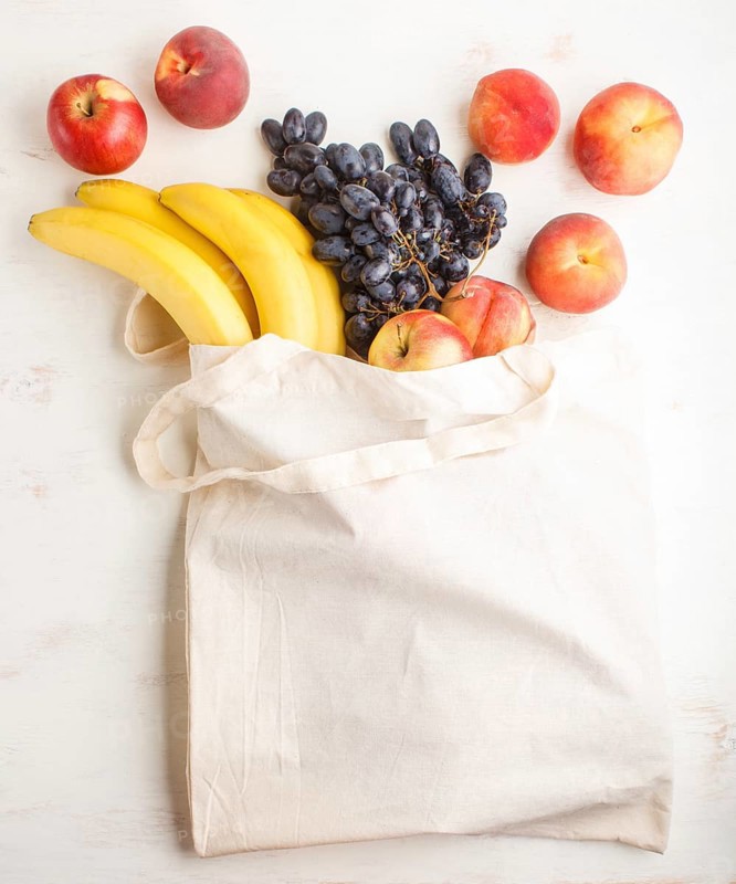 Fruits in reusable cotton textile white bag. Zero waste shopping, storage and recycling concept, eco friendly lifestyle. Top view, flat lay, copy space. Peach, apple, banana, grape