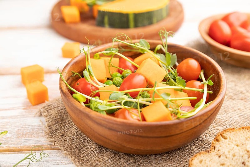 Vegetarian vegetable salad of tomatoes, pumpkin, microgreen pea sprouts on white wooden background and linen textile. Side view, close up, selective focus