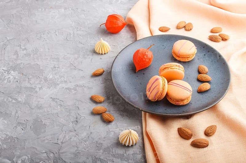 Orange macarons or macaroons cakes on blue ceramic plate on a gray concrete background and orange textile. side view, copy space