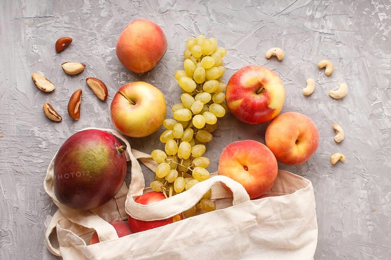 Fruits in reusable cotton textile white bag. Zero waste shopping, storage and recycling concept, eco friendly lifestyle. Top view, flat lay, close up. Peach, apple, nuts, mango, grape