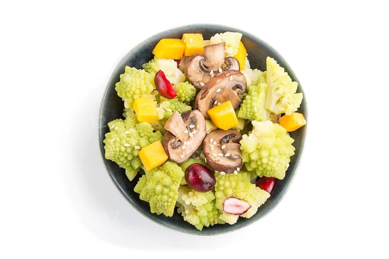 Vegetarian salad from romanesco cabbage, champignons, cranberry, avocado and pumpkin in black bowl isolated on a white background. top view, close up, flat lay