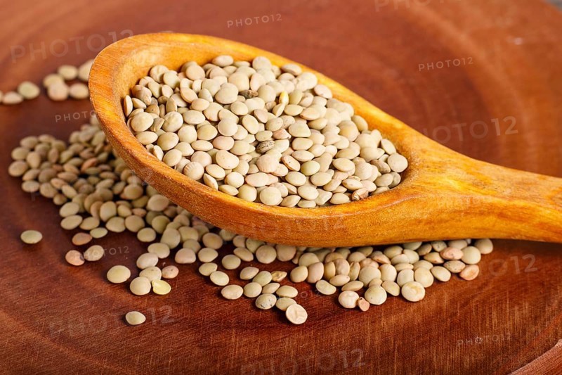 Pile of green lentils in a wooden spoon on brown background. Closeup