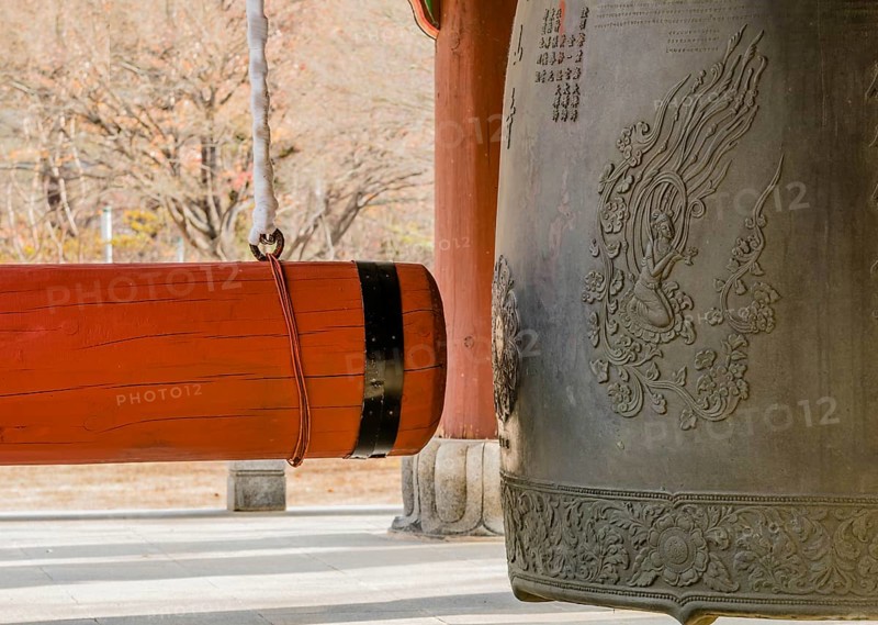 Large red wooden gong on linen wrapped chain hanging next to traditional metal Buddhist temple bell in South Korea