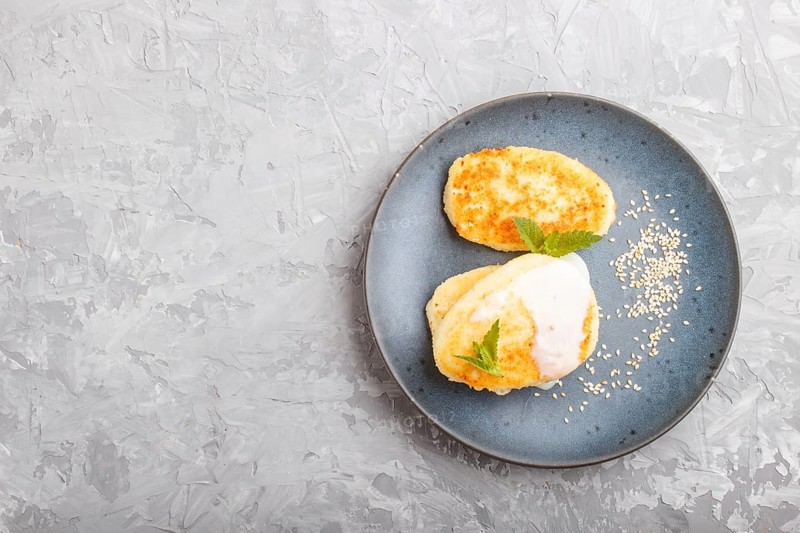 Cheese pancakes on a blue ceramic plate with milk sauce on a gray concrete background. top view, flat lay, copy space