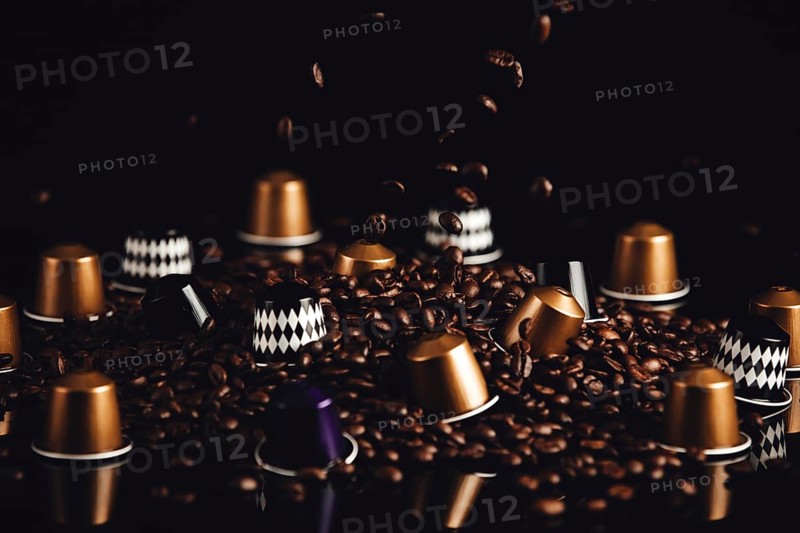 Scattered coffee capsules and coffee beans with falling coffee beans on a dark background