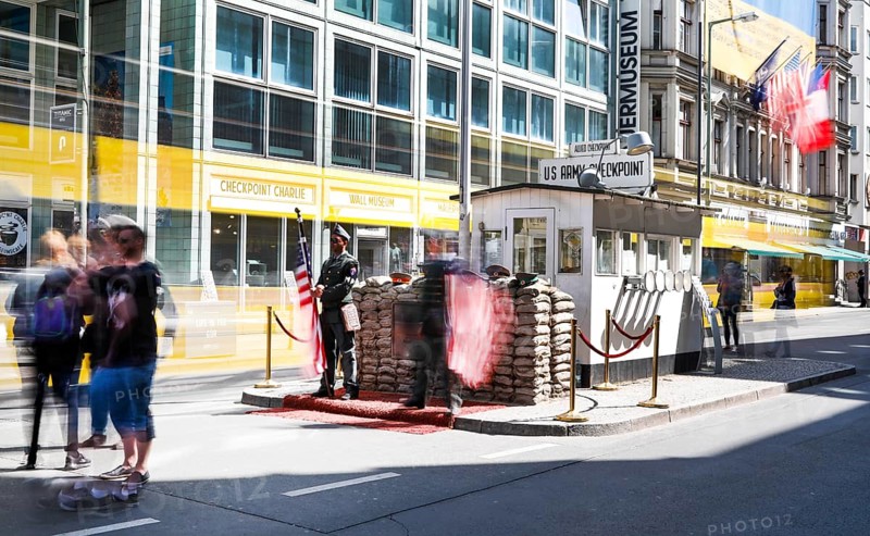 A long exposure shows a tourist at Checkpoint Charlie, men in American military uniforms stand in the guardhouse, Berlin 04.05.2018