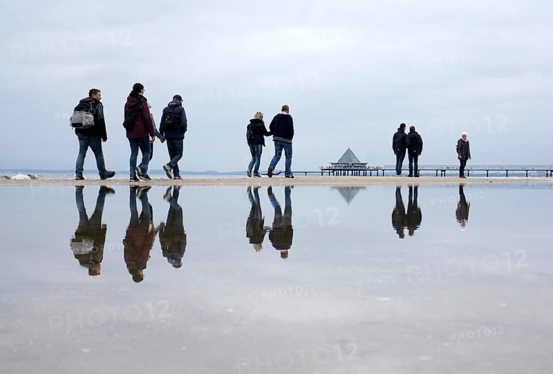 Walkers reflected in the water on the beach in Heringsdorf, Usedom Island, 21/09/2019