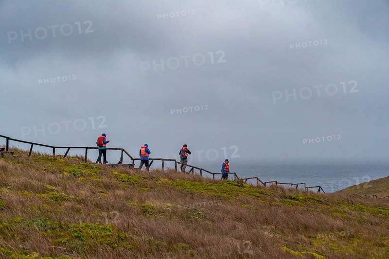 Passengers of the cruise ship Stella Australis in life jackets hike in storm and rain to Cape Horn, southernmost point of America, Horn Island, Cabo de Hornos National Park, Tierra del Fuego, Patagonia, Chile, South America