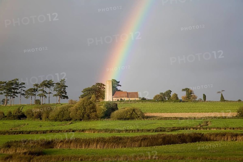The end of a rainbow lights up the tower of All Saints church, Ramsholt, Suffolk, England, United Kingdom, Europe