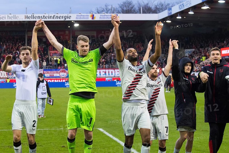 Football match, the Bayer Leverkusen players from left to right: Josip STANISIC, goalkeeper and captain Lukas HRADECKY, Jonathan TAH, Jonas HOFMAN hidden, Florian WIRTZ and Patrik SCHICK celebrate the victory with their travelling fans in the fan curve, Voith-Arena football stadium, Heidenheim