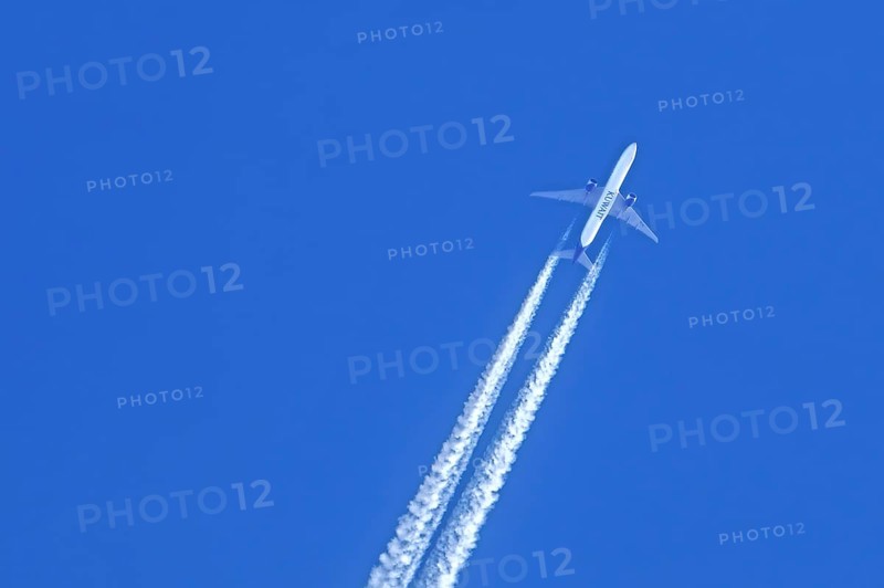 Flying twin-engine jet airliner, aircraft, plane from the airline Kuwait Airways showing contrails, condensation trails against blue sky