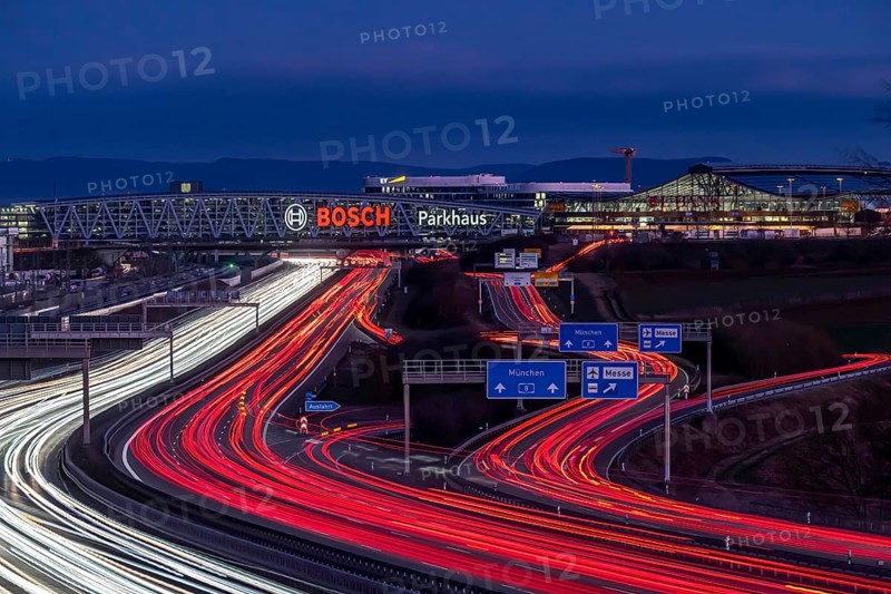 A8 motorway at Stuttgart Airport with Bosch multi-storey car park in the evening, cars create light trails. The 440 metre long construction offers space for 4200 vehicles. Bosch owns the naming rights, the stylised ignition anchor measures 12 metres in diameter. This makes it one of the largest neon signs in the world. Stuttgart, Baden-Wuerttemberg, Germany, Europe