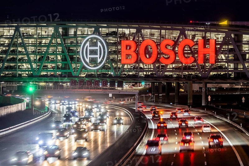 A8 motorway at Stuttgart Airport with Bosch multi-storey car park in the evening, cars create light trails. The 440 metre long construction offers space for 4200 vehicles. Bosch owns the naming rights, the stylised ignition anchor measures 12 metres in diameter. This makes it one of the largest neon signs in the world. Stuttgart, Baden-Wuerttemberg, Germany, Europe