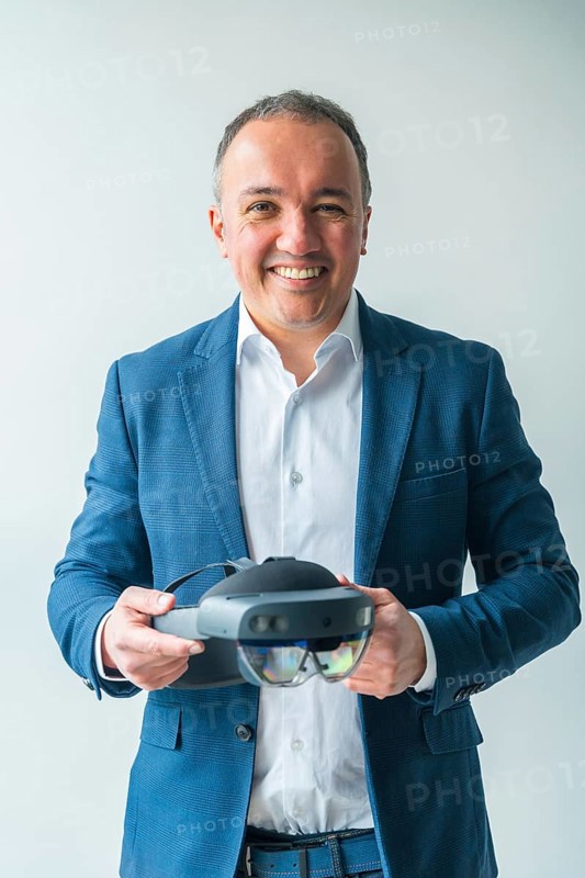 Vertical studio portrait with grey background of a confident businessman holding a futuristic mixed reality goggles