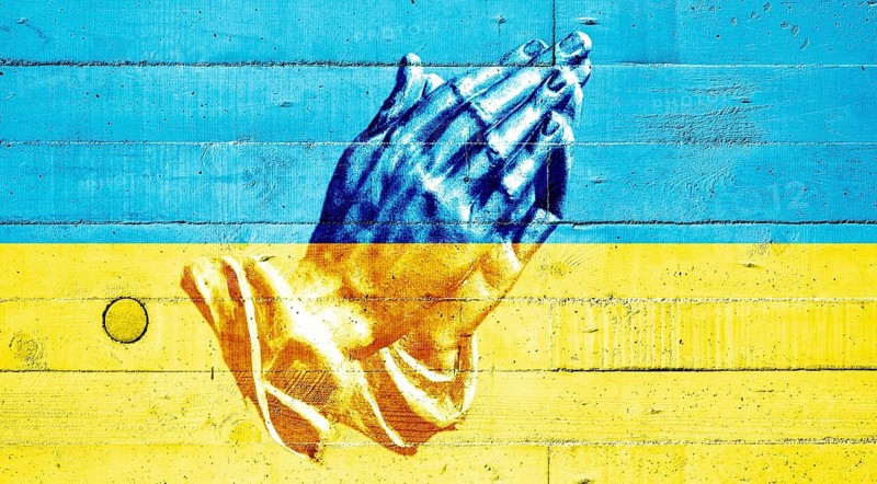 Ukrainian flag painted on a concrete wall with praying hands
