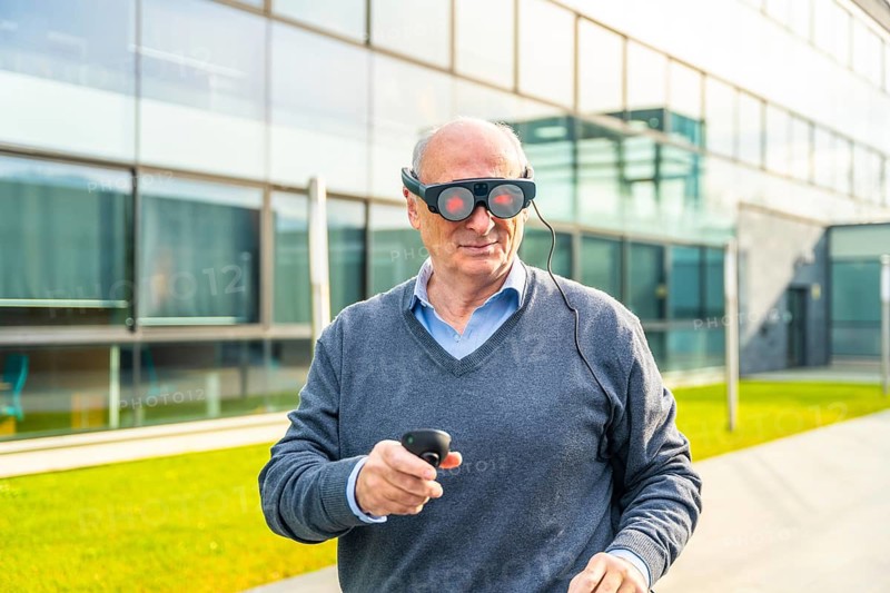 Smiling elder businessman using an augmented reality device outside the financial building